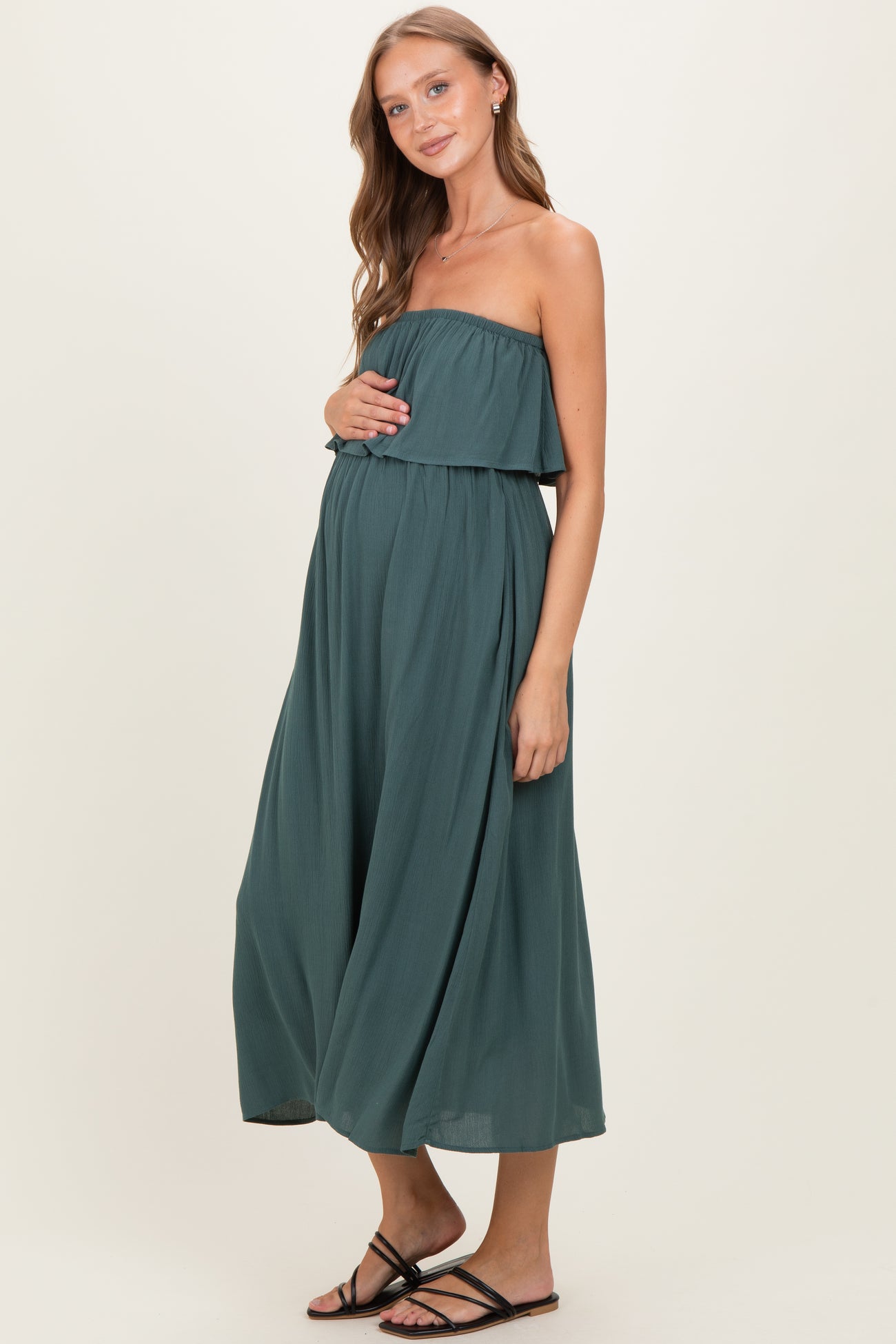 woman wearing a dark green strapless maternity maxi dress and holding her baby bump