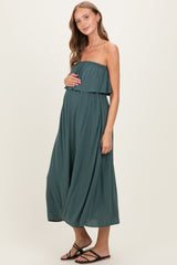 woman wearing a dark green strapless maternity maxi dress and holding her baby bump