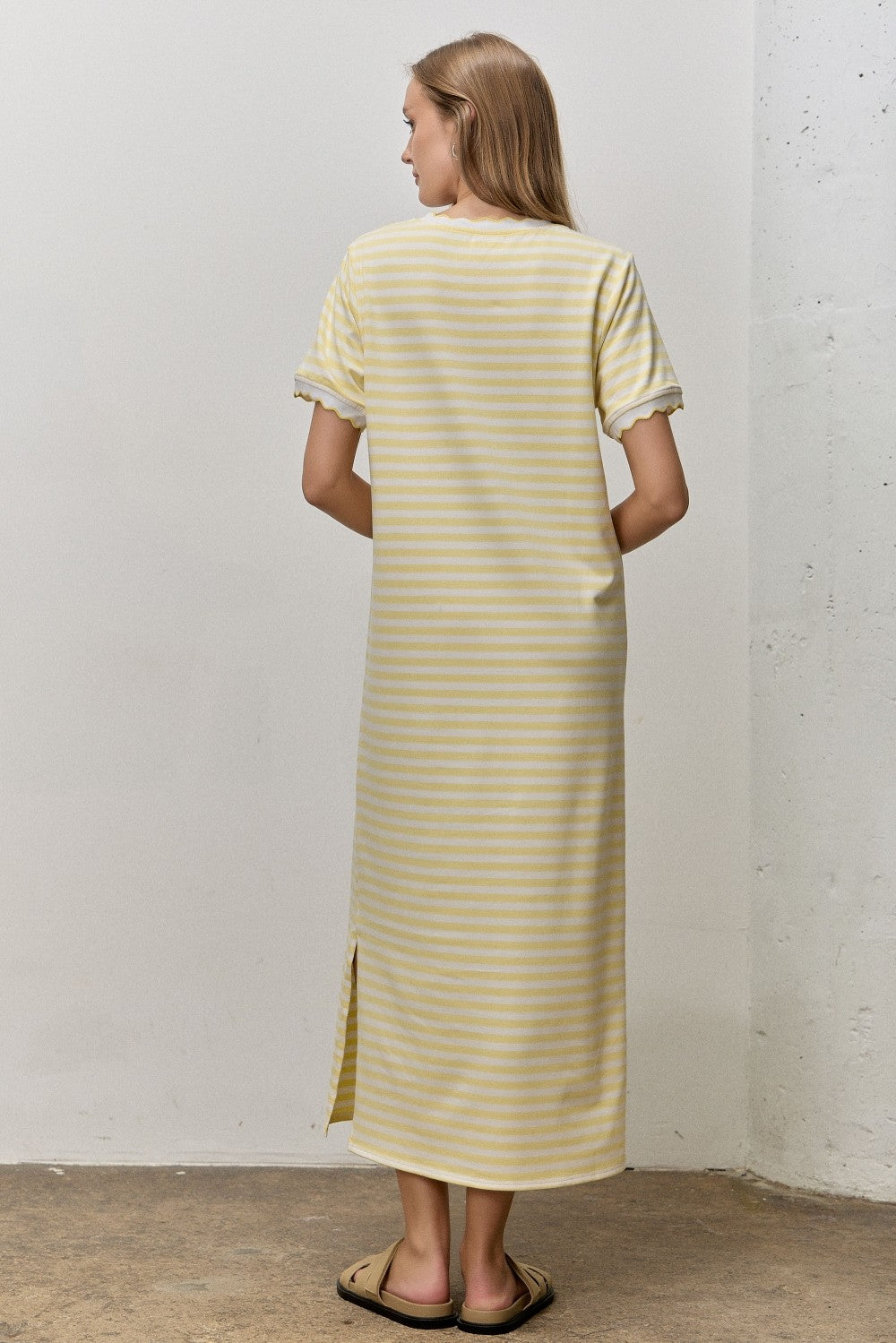 woman wearing a yellow and white striped maxi dress with short sleeves and side slit, viewed from the back