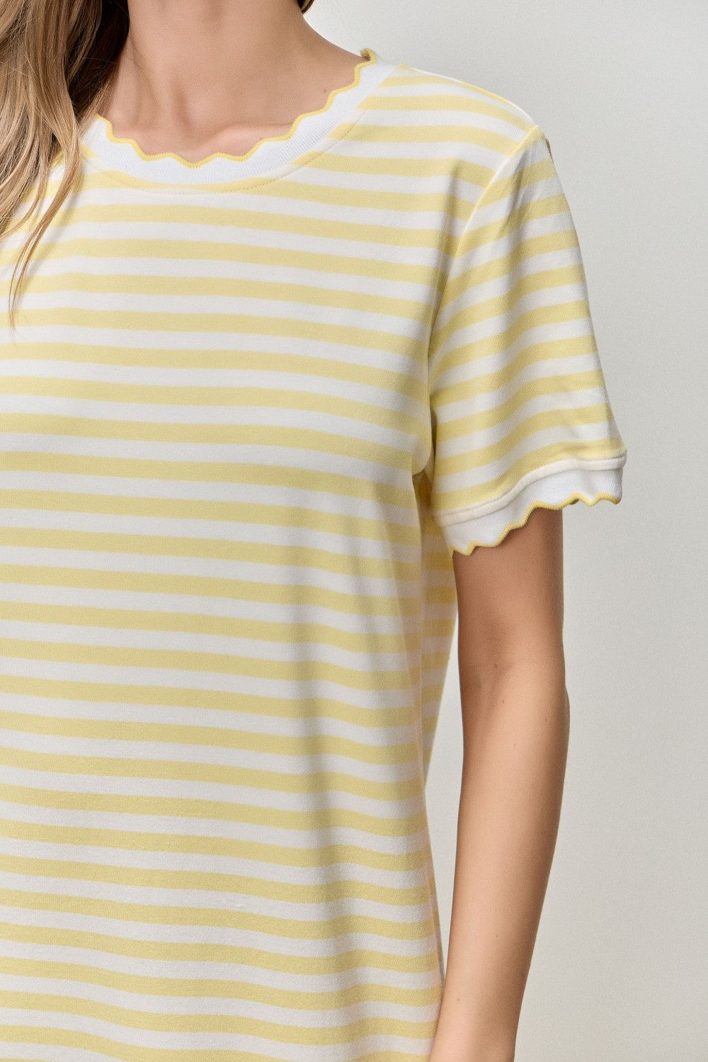woman wearing a yellow and white striped short sleeve top with scalloped neckline and sleeve edges