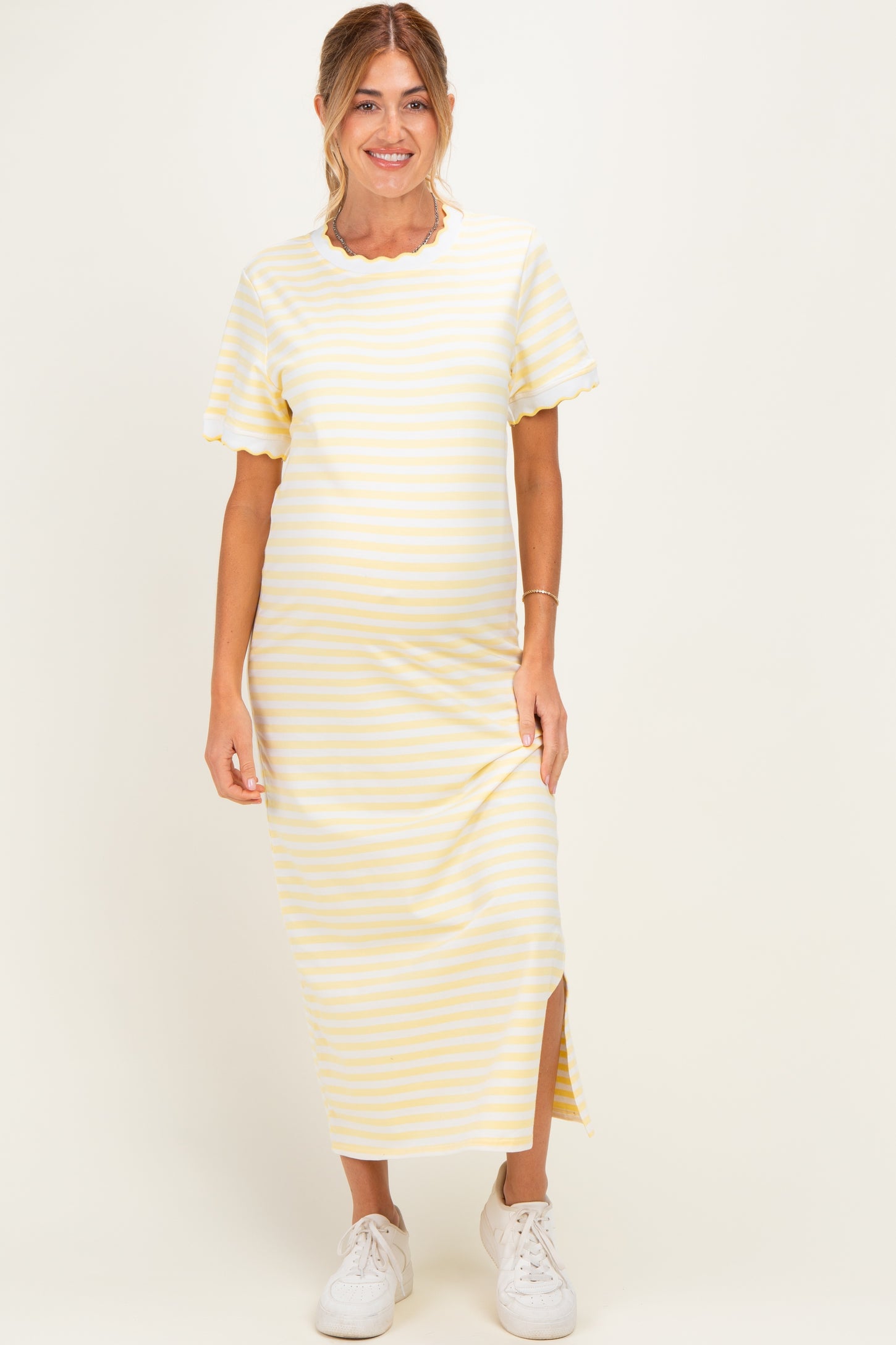 woman wearing a yellow and white striped maternity maxi dress with short sleeves and a side slit, showing her baby bump