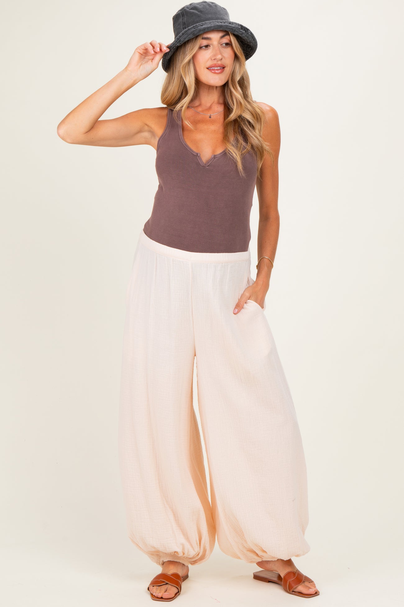 woman wearing a mauve ribbed maternity tank top and cream balloon pants with pockets, accessorized with a gray bucket hat