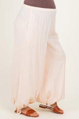 woman wearing light peach maternity harem pants with pockets and elastic cuffs at the ankles, styled with brown sandals