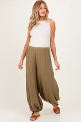 woman wearing a cream tank top and olive green maternity wide-leg pants, walking with a casual pose