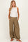 woman wearing a white tank top and olive green maternity wide-leg pants with side pockets and drawstring hems