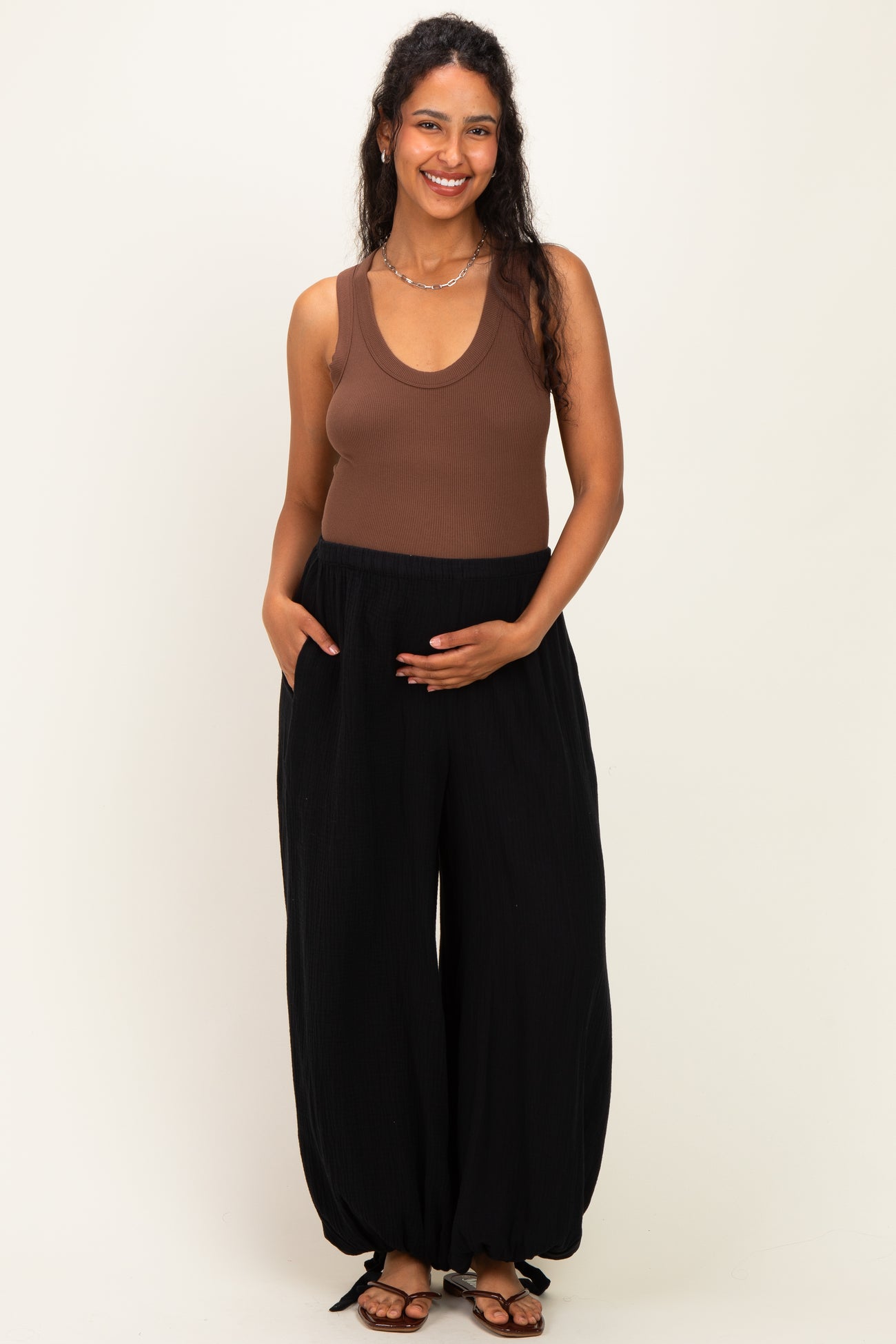 woman wearing a brown ribbed maternity tank top and black maternity wide-leg pants, holding her baby bump