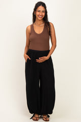 woman wearing a brown ribbed maternity tank top and black maternity wide-leg pants, holding her baby bump