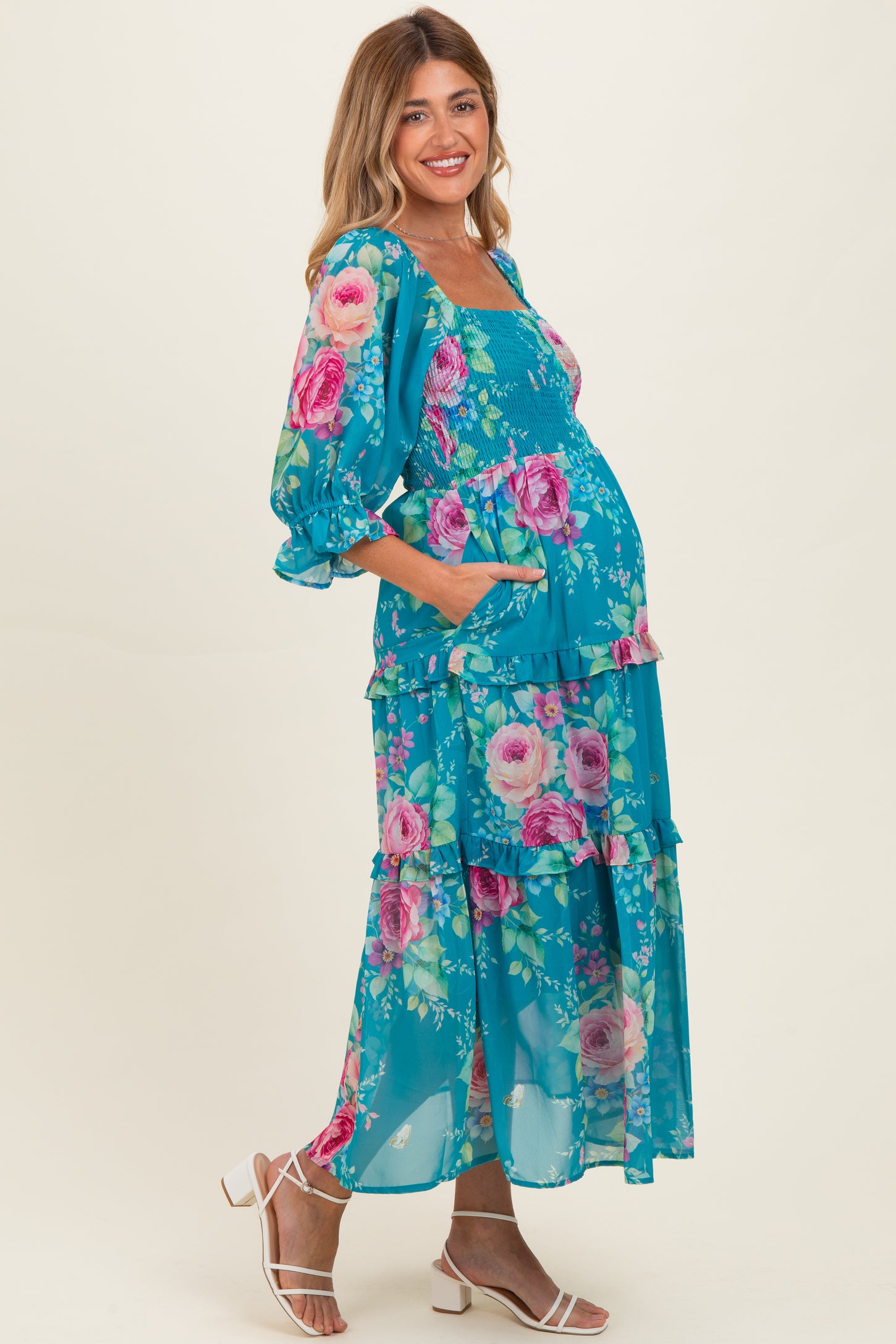 woman wearing a turquoise floral maternity dress with tiered ruffles and a smocked bodice, showcasing her baby bump