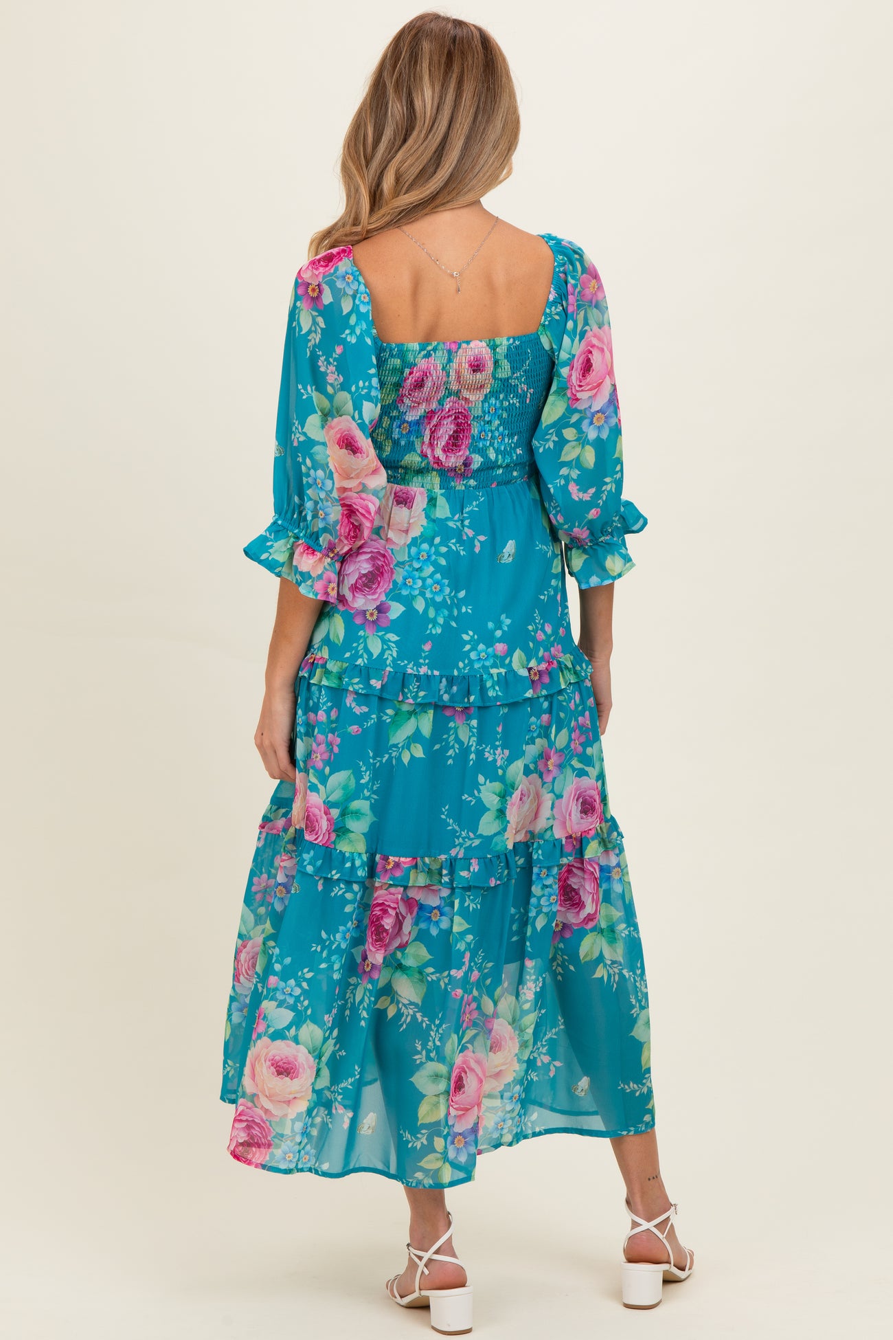 woman wearing a flowy teal floral maternity maxi dress with ruffled sleeves and tiered skirt, showing her baby bump from behind