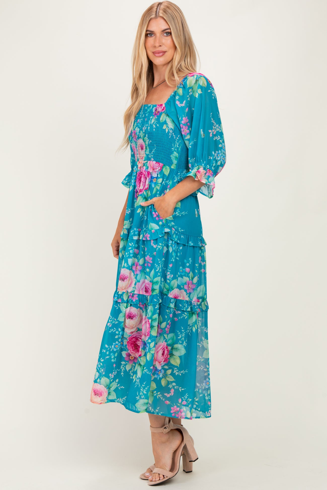 woman wearing a teal floral maxi dress with puff sleeves and pockets, standing against a neutral background