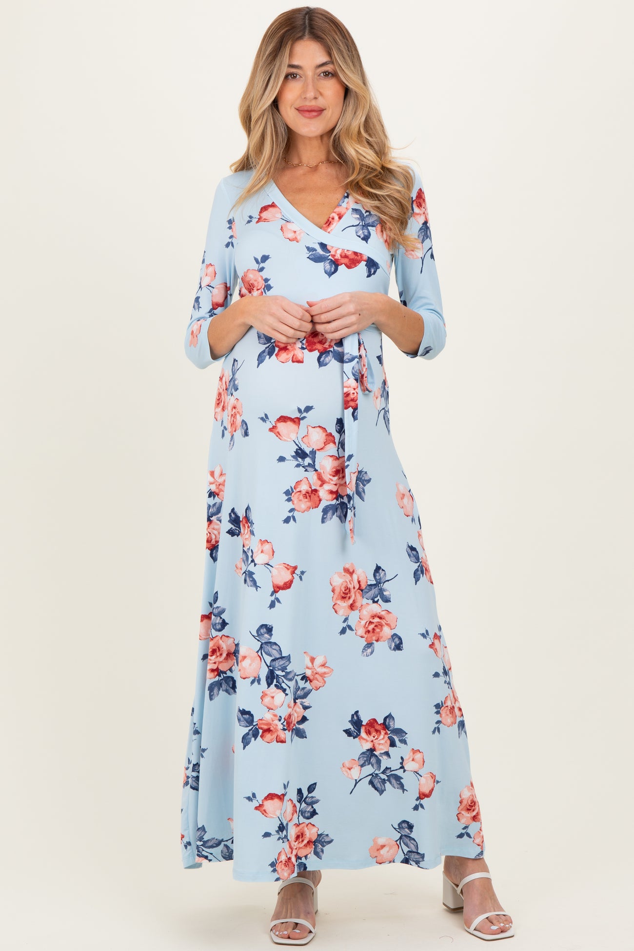 woman wearing a light blue floral maternity maxi dress with three-quarter sleeves and a v-neckline, holding her baby bump