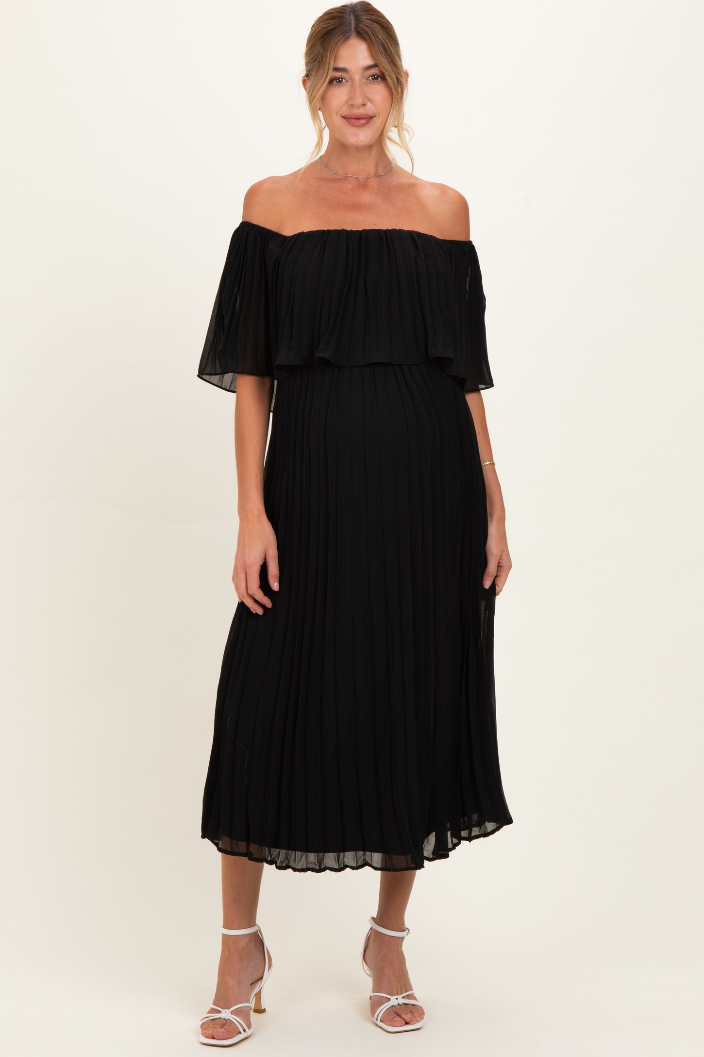 woman wearing a black off-the-shoulder pleated maternity dress with a flowing design and standing in a relaxed pose