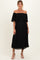 woman wearing a black off-the-shoulder pleated maternity dress with a flowing design and standing in a relaxed pose