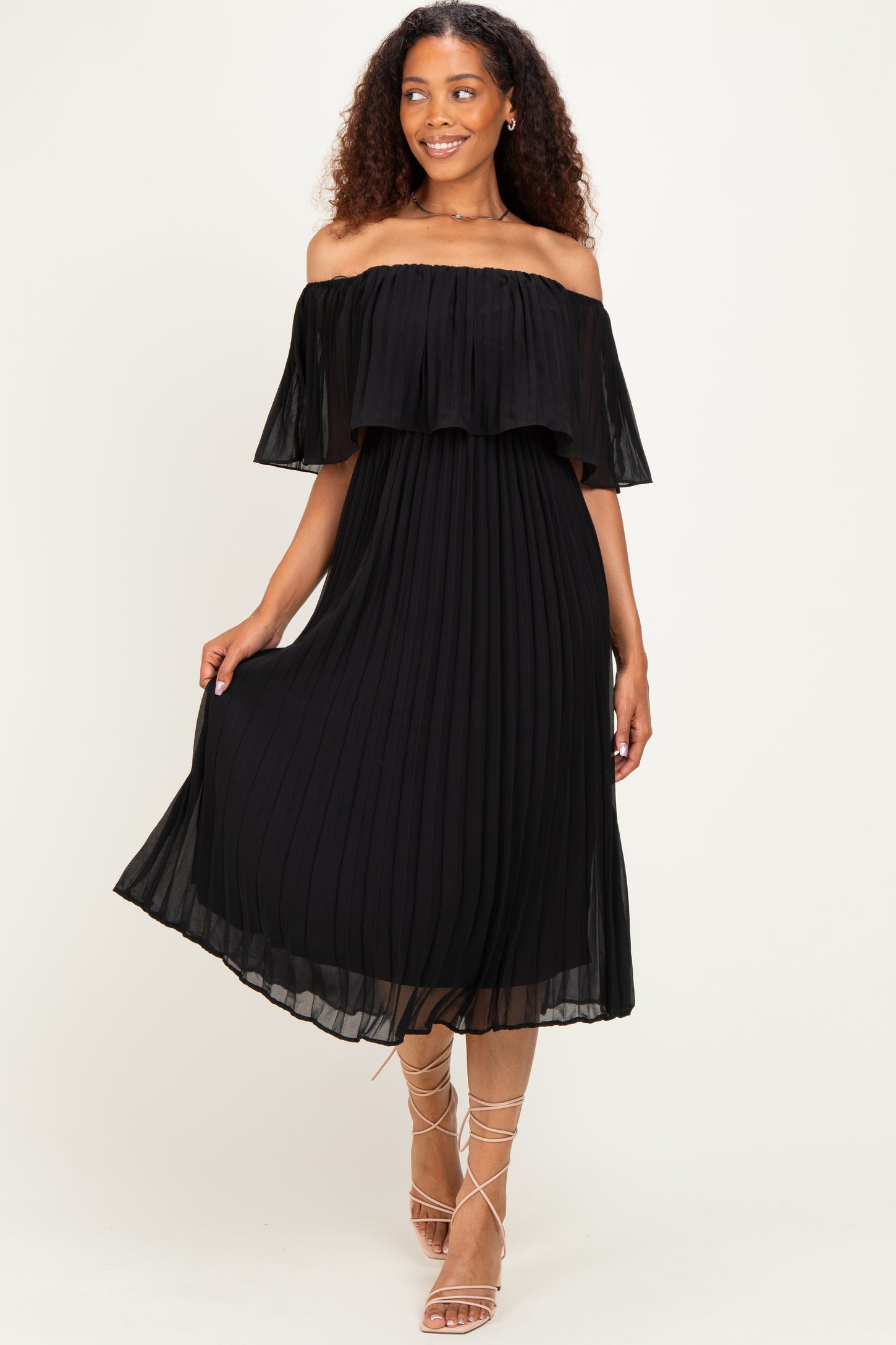 woman wearing a black off-shoulder pleated midi dress with ruffle details and strappy sandals