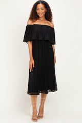 woman wearing a black off-the-shoulder pleated dress with a flowing ruffle detail and strappy sandals