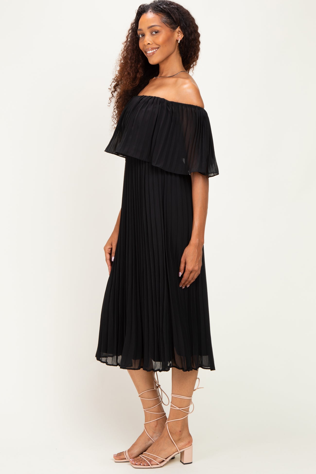 woman wearing a black off-the-shoulder pleated midi dress with a flowy silhouette and matching sandals