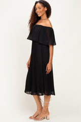 woman wearing a black off-the-shoulder pleated midi dress with a flowy silhouette and matching sandals