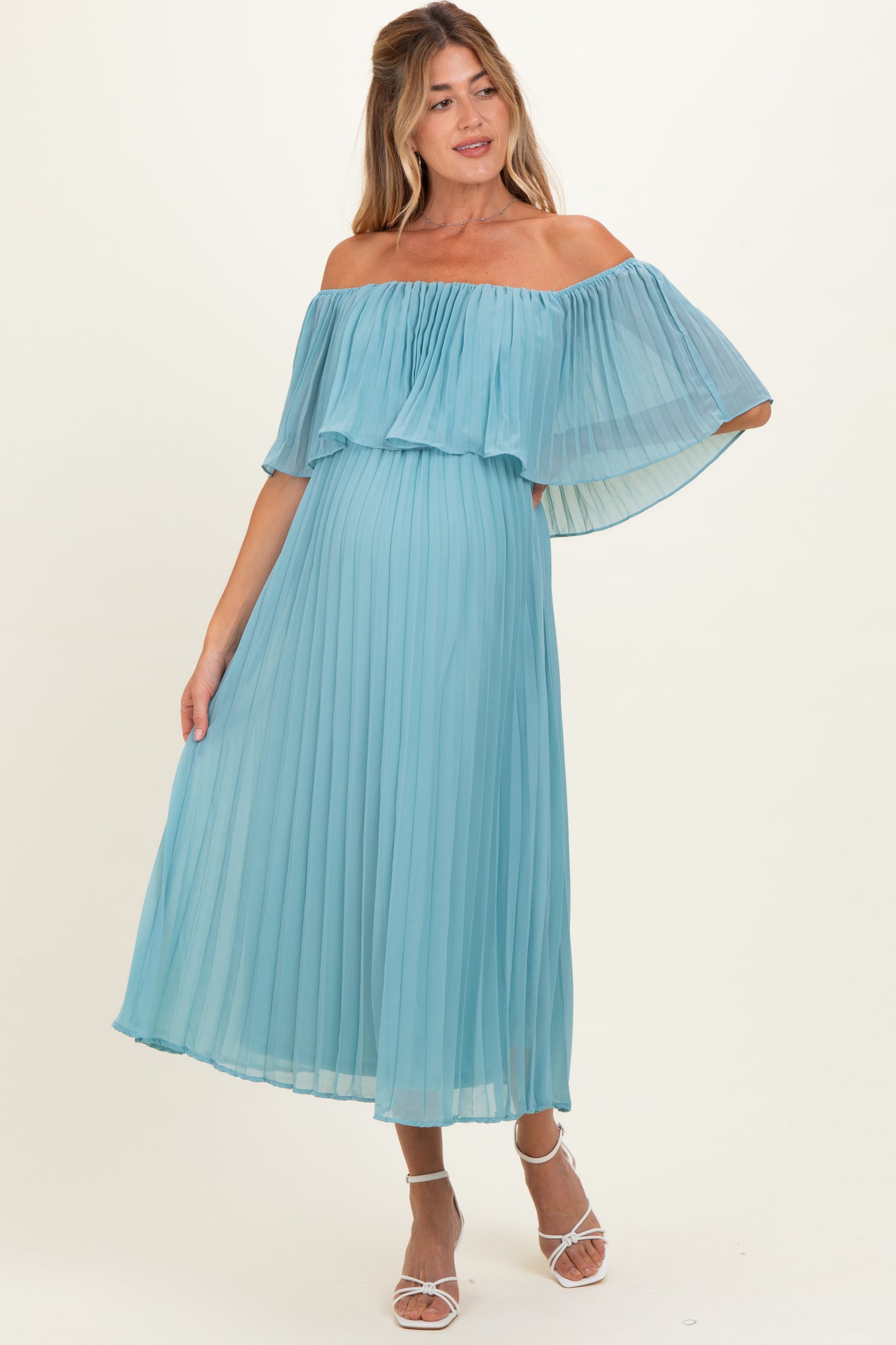woman wearing a light blue off-the-shoulder pleated maternity dress with flowing sleeves and a visible baby bump
