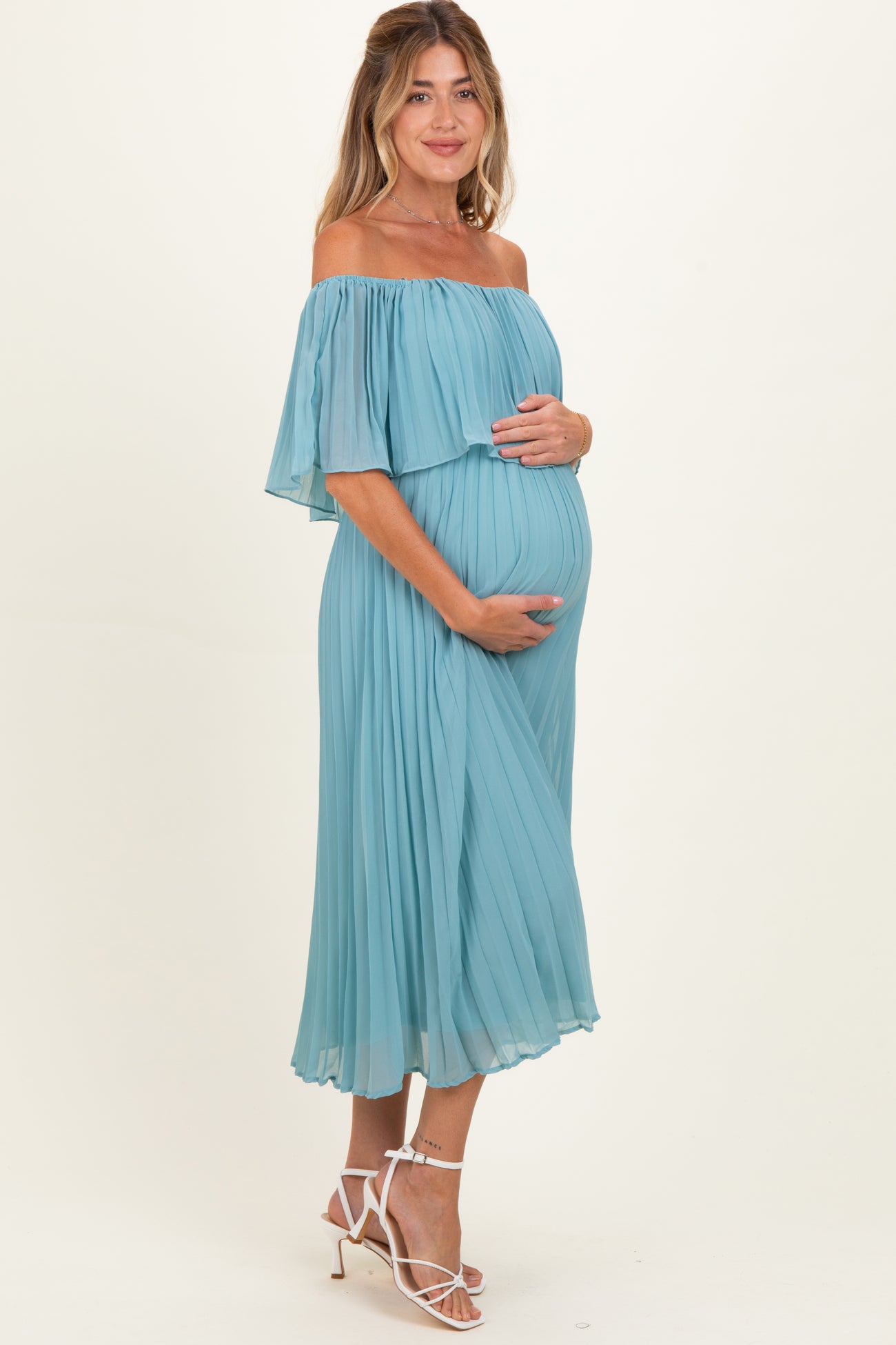 woman wearing a light blue off-the-shoulder maternity dress and holding her baby bump
