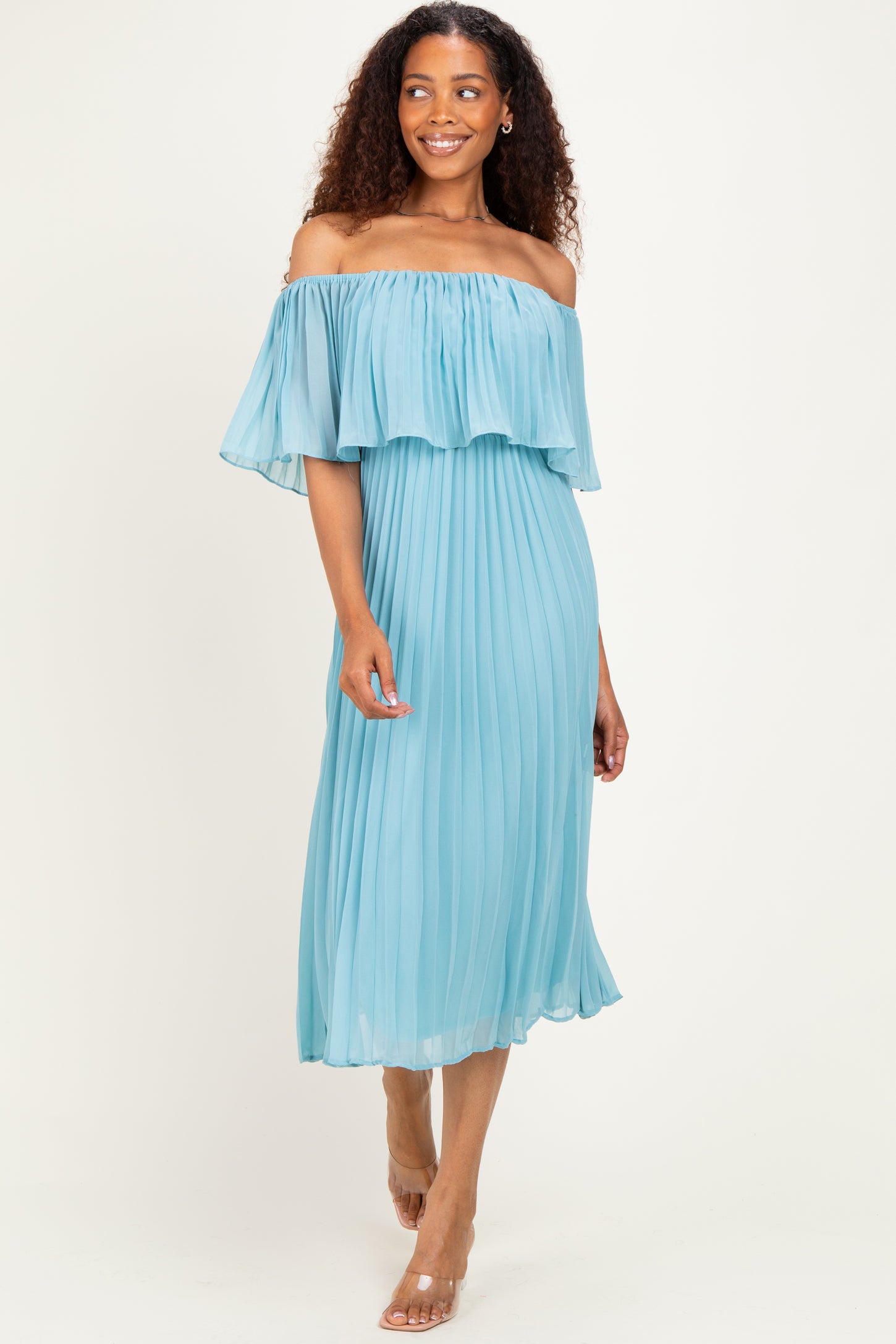 woman wearing a light blue off-the-shoulder pleated dress with ruffle detailing and flowing sleeves