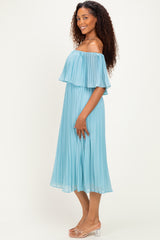 woman wearing a light blue off-the-shoulder pleated dress, standing in profile with a flowy silhouette