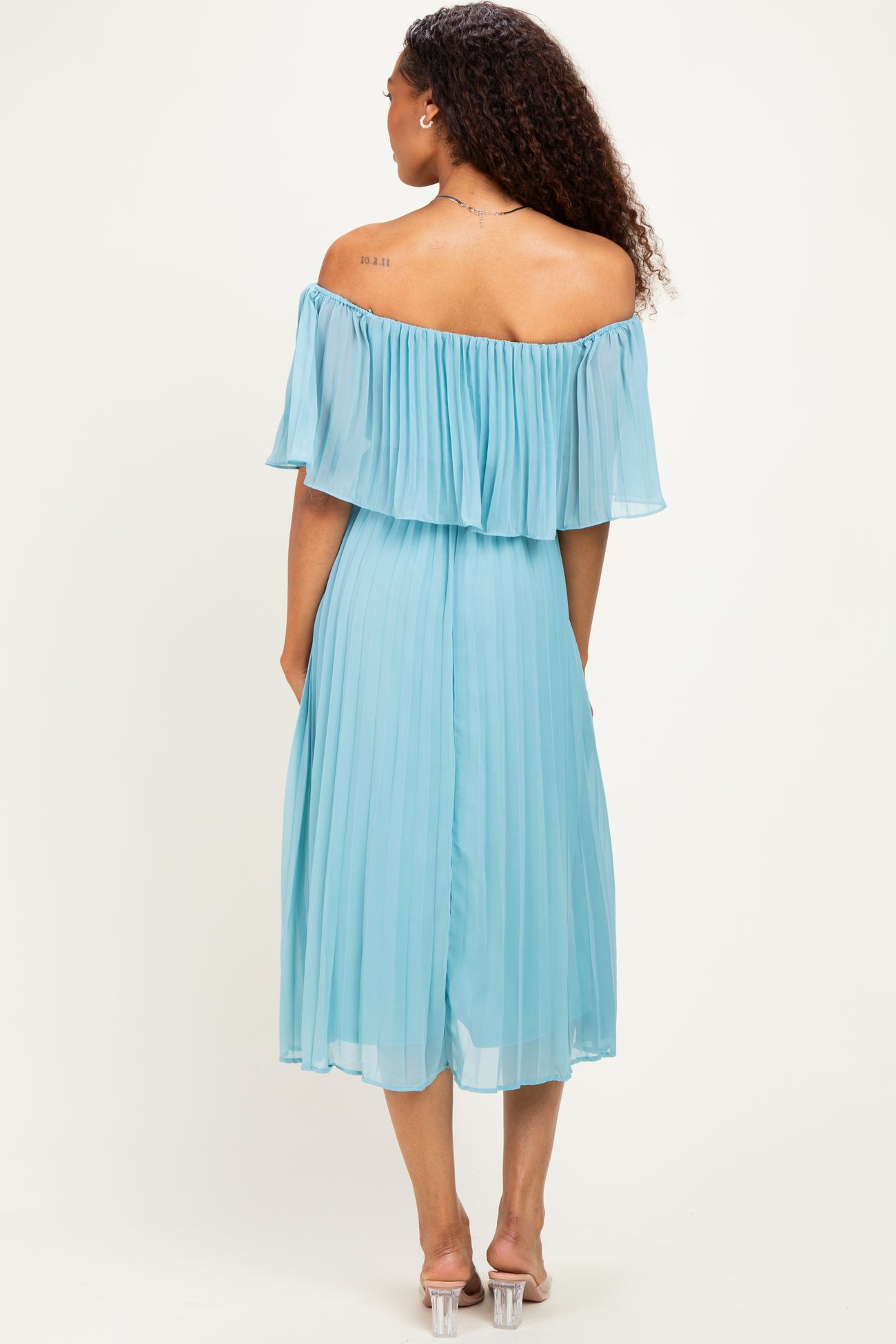 woman wearing a light blue off-the-shoulder pleated dress, standing with her back to the camera