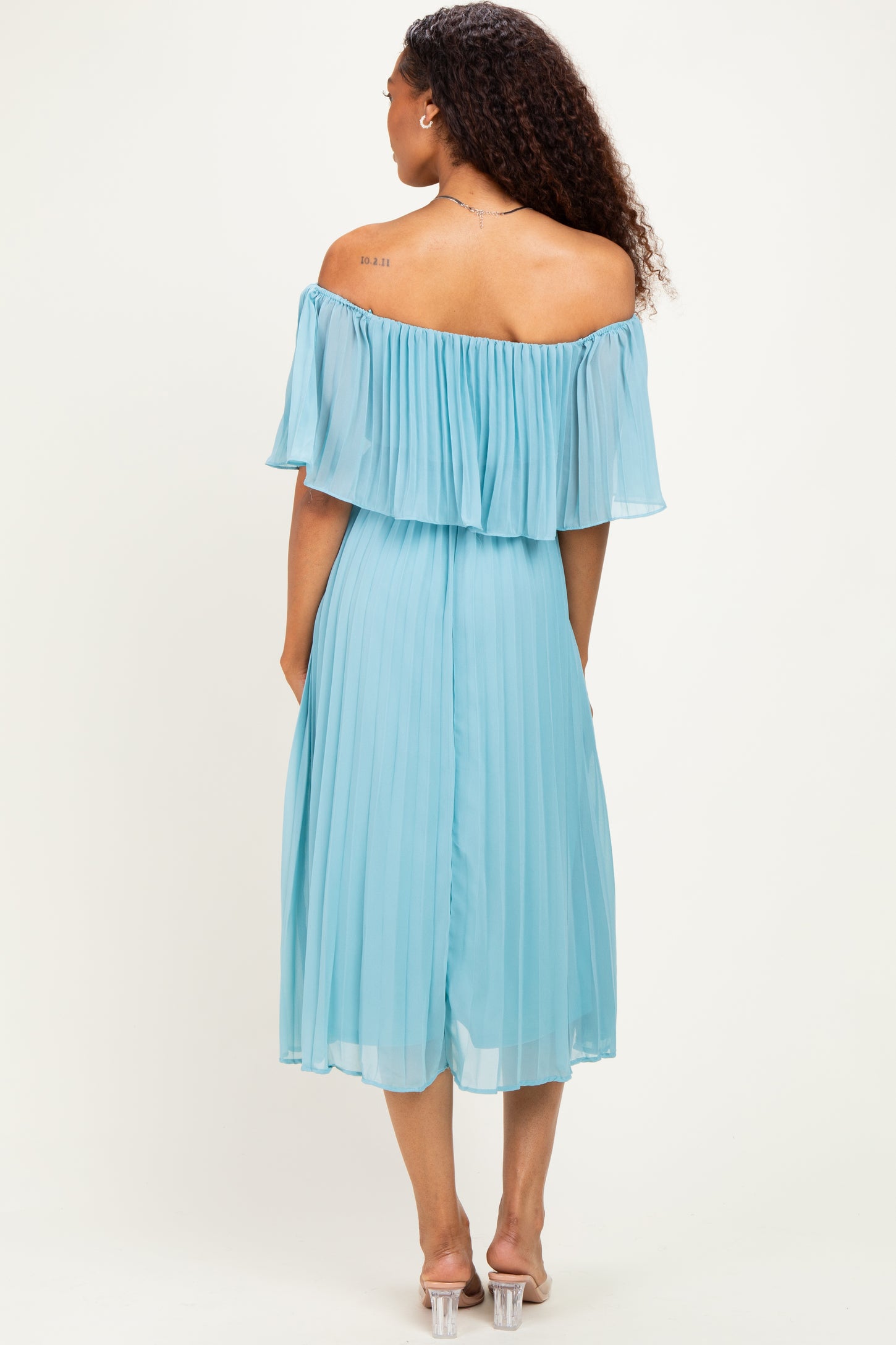 woman wearing a light blue off-the-shoulder pleated dress, standing with her back to the camera