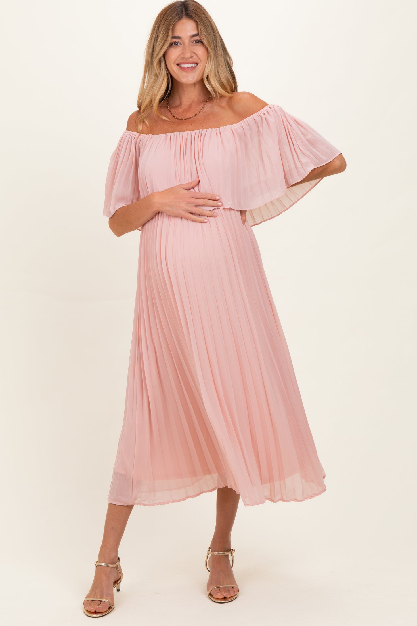 woman wearing a pink off-the-shoulder pleated maternity dress and holding her baby bump