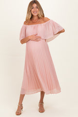 woman wearing a pink off-the-shoulder pleated maternity dress and holding her baby bump