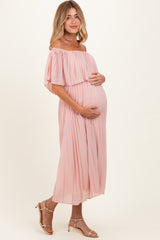 woman wearing a light pink off-the-shoulder maternity dress and holding her baby bump