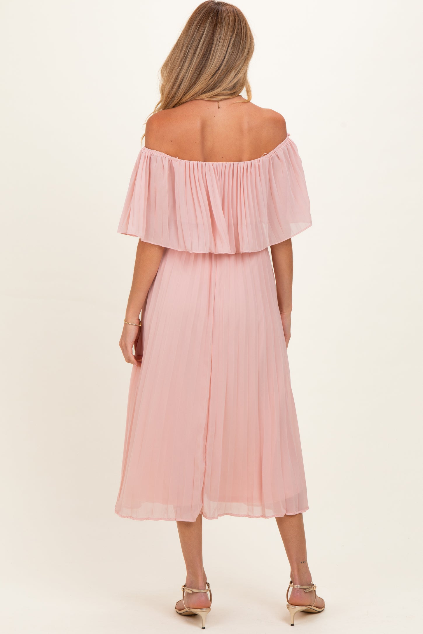 woman wearing a light pink off-the-shoulder maternity dress with pleated details, showing a pregnant baby bump from the back
