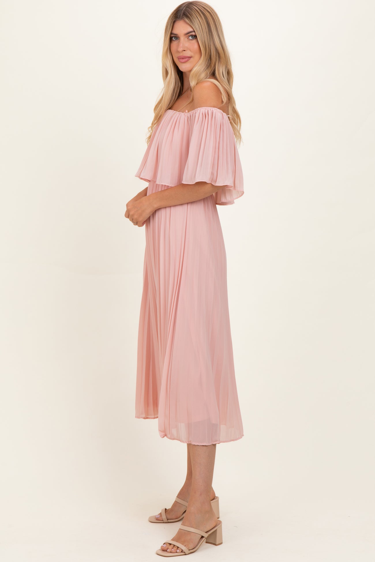woman wearing a light pink off-the-shoulder pleated midi dress with flowing sleeves and a relaxed fit