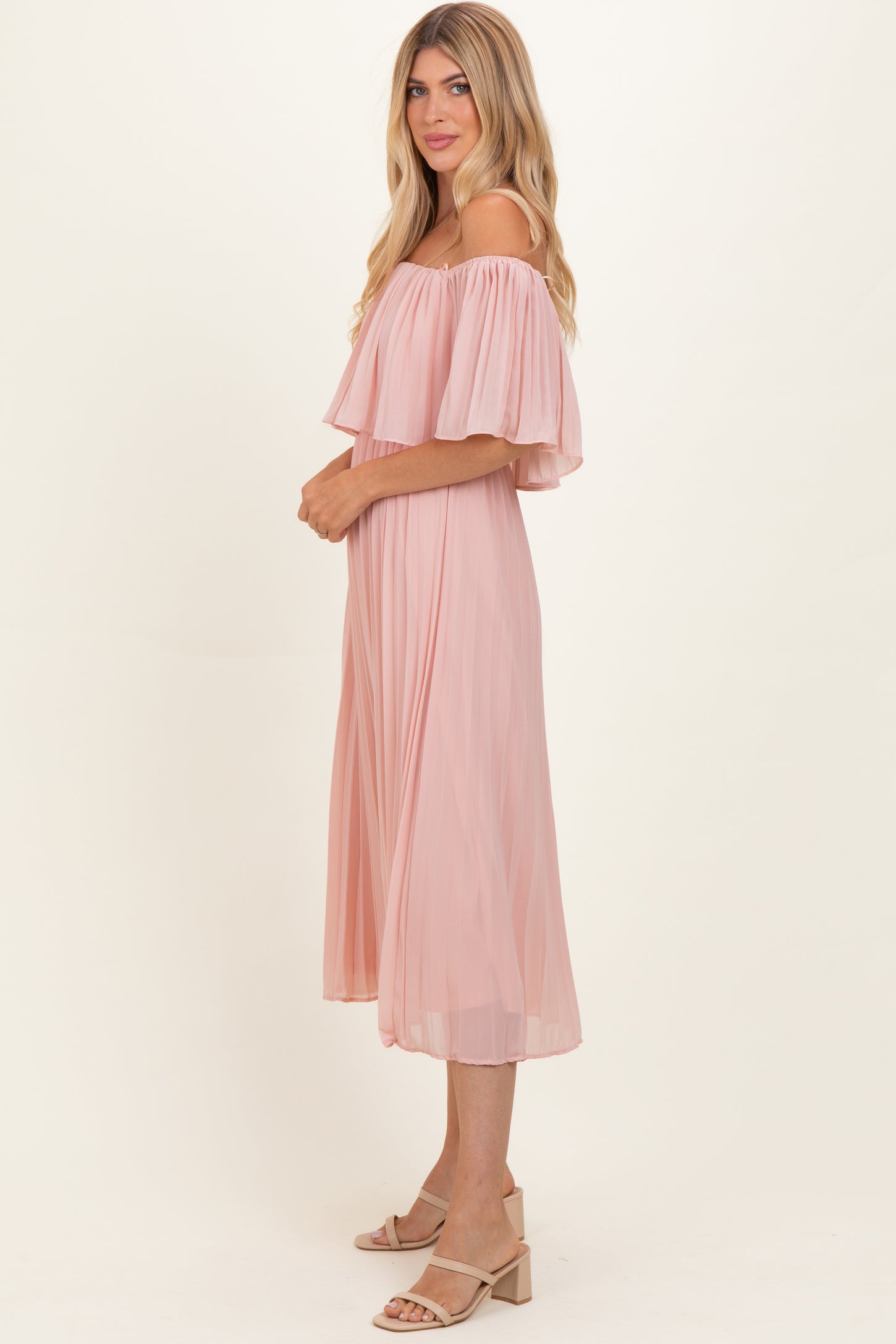 woman wearing a light pink off-the-shoulder pleated midi dress with flowing sleeves and a relaxed fit