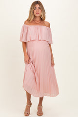 woman wearing a blush pink off-the-shoulder pleated maternity dress with a visible baby bump