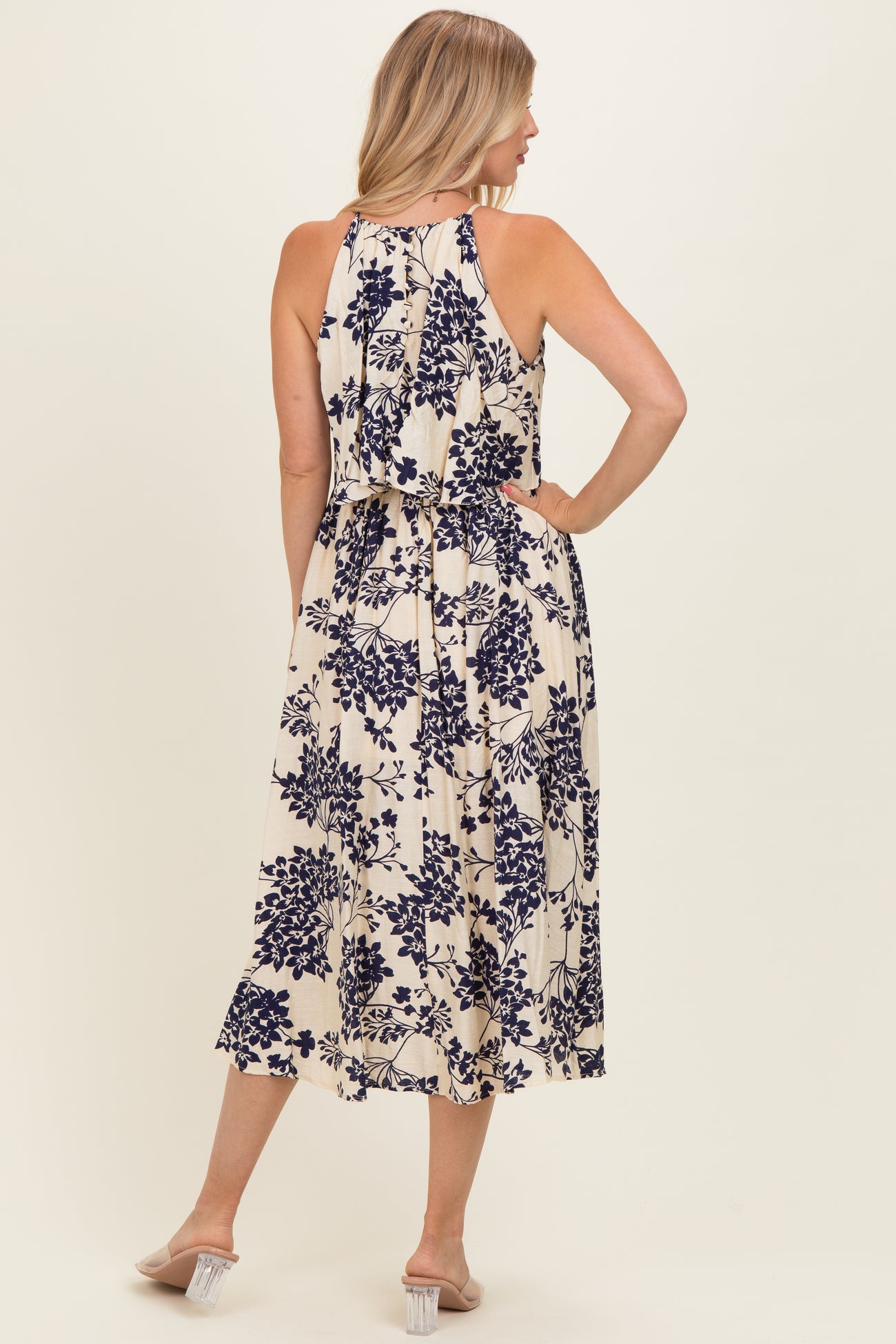woman wearing a sleeveless cream floral midi dress with a tiered design and back tie detail