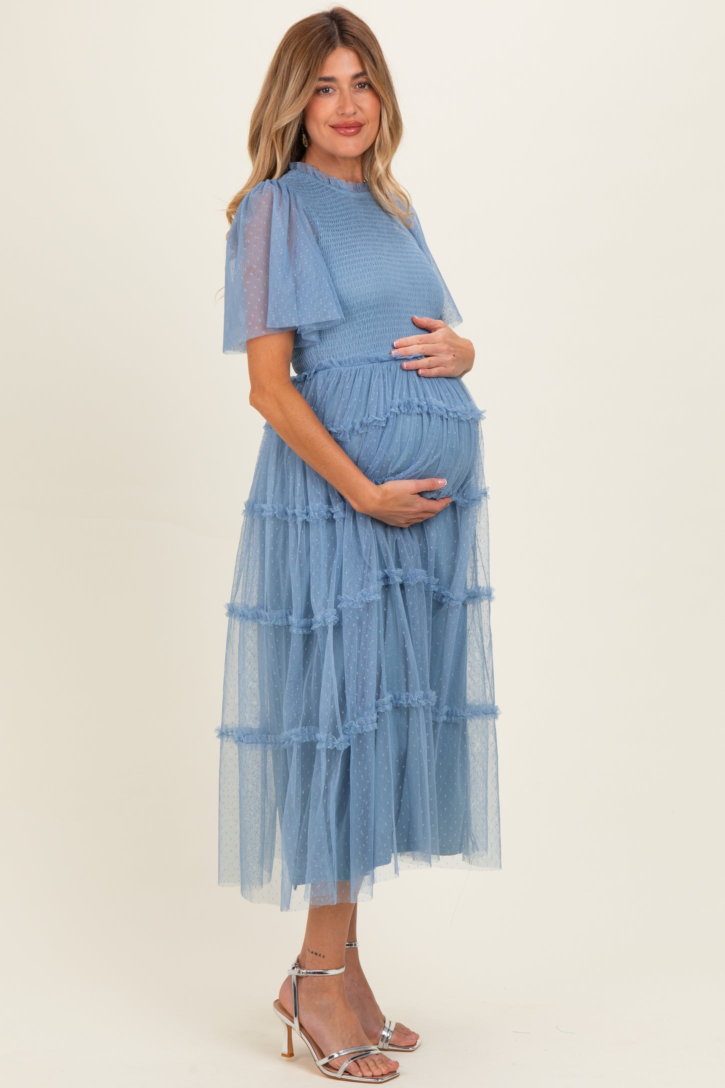 woman wearing a light blue maternity dress with tiered tulle layers and puff sleeves, showing her baby bump