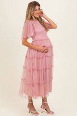 woman wearing a pink maternity dress with short puff sleeves and layered tulle skirt, cradling her baby bump