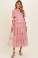 woman wearing a pink maternity dress with ruffled tulle layers and short puff sleeves, holding her baby bump