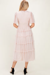 woman wearing a light pink tiered tulle midi dress with short puff sleeves and a fitted bodice