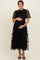 woman wearing a black maternity dress with layered tulle skirt and sheer puff sleeves, holding her baby bump