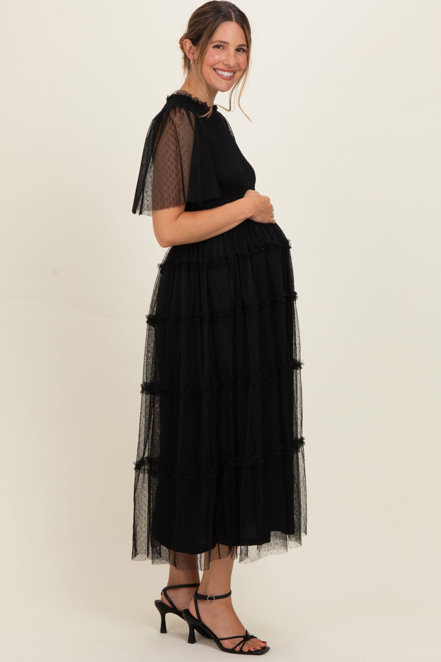 woman wearing a black maternity maxi dress with tiered tulle ruffles, showing her baby bump