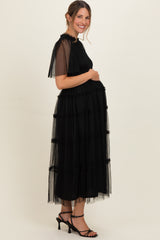 woman wearing a black maternity maxi dress with tiered tulle ruffles, showing her baby bump
