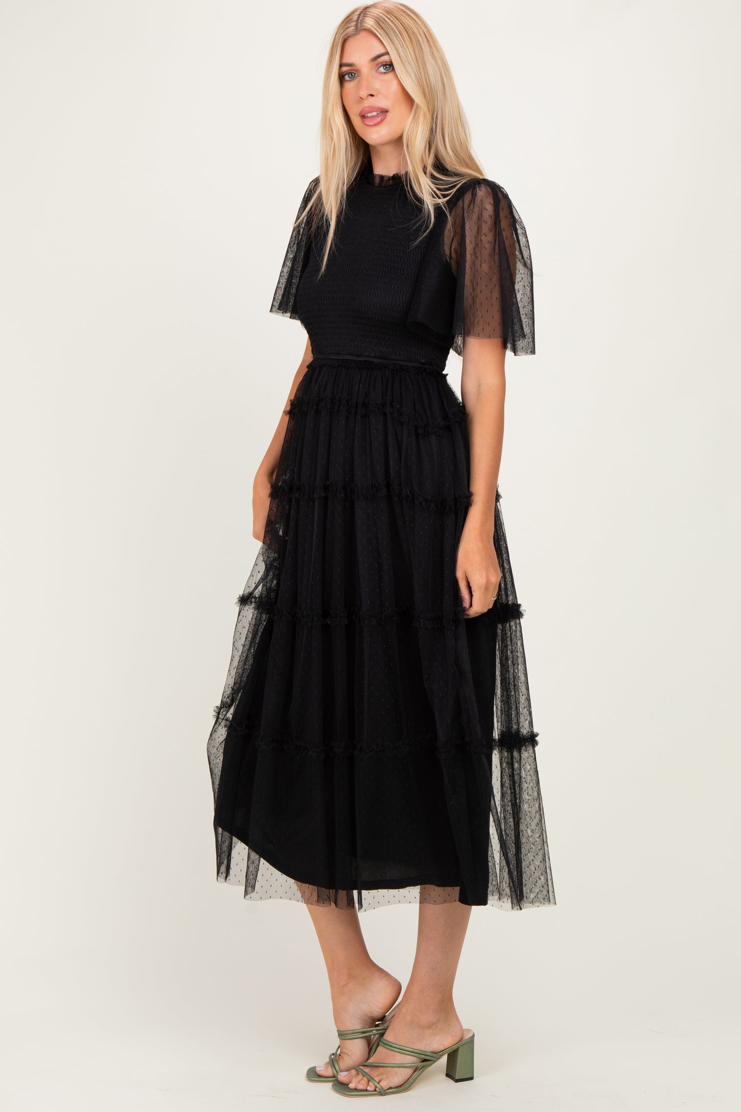 woman wearing a black tiered maxi dress with sheer puff sleeves and a fitted bodice, standing in sandals