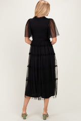 woman wearing a black tiered tulle dress with short sleeves, viewed from the back, showcasing a flowy silhouette