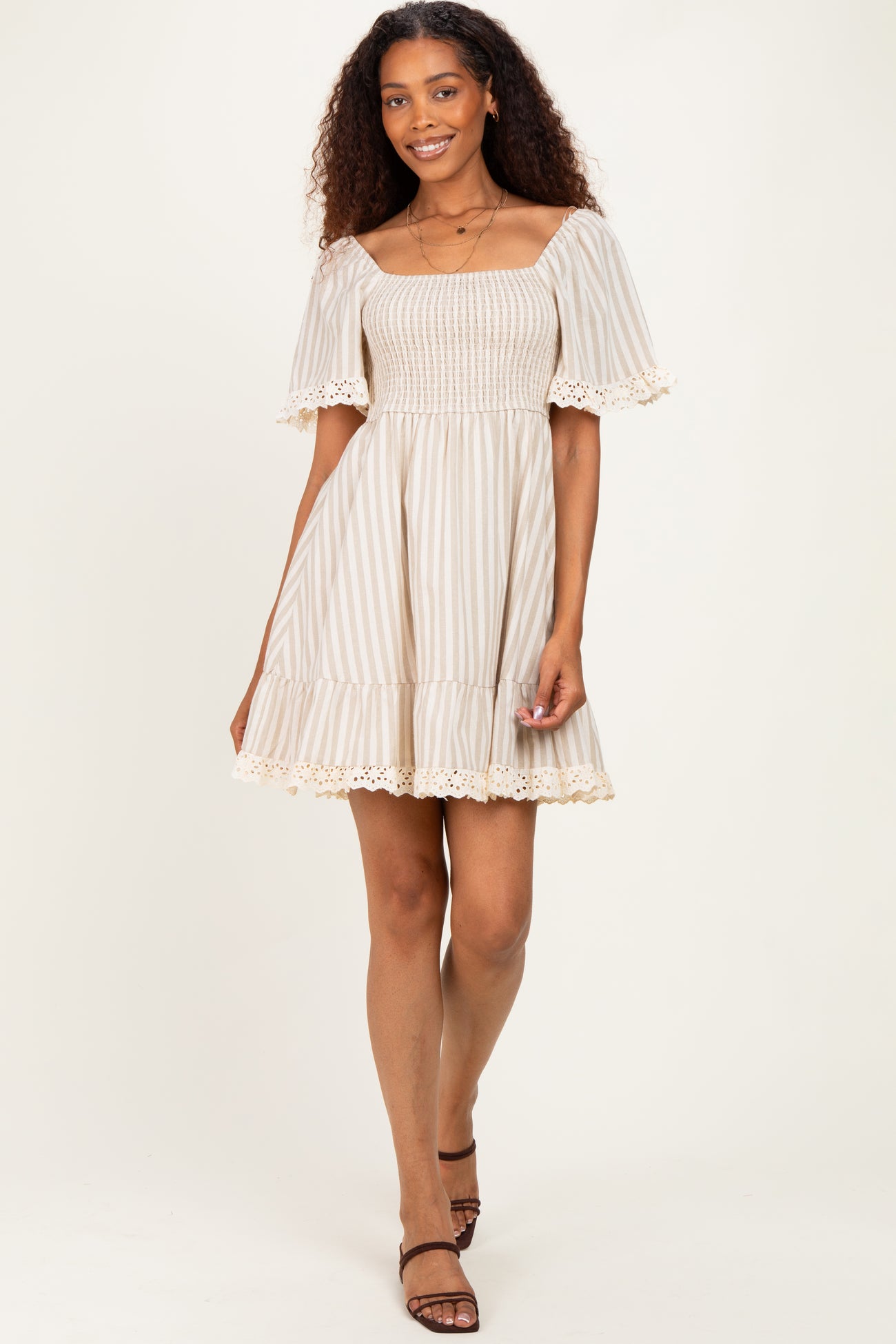 woman wearing a cream and beige striped off-the-shoulder dress with smocking and lace trim