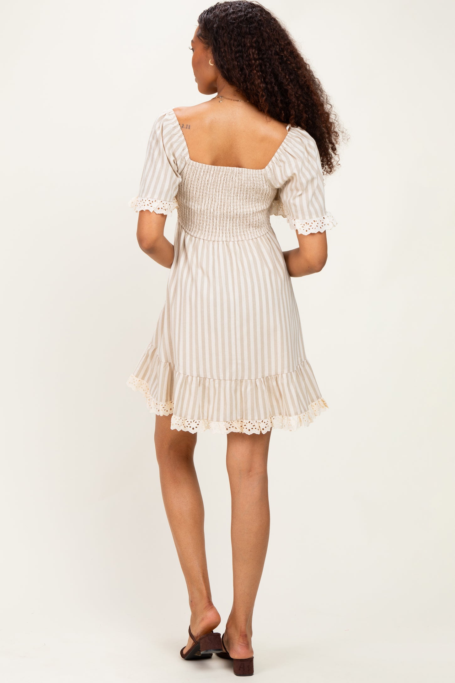 woman wearing a beige and white striped mini dress with short puff sleeves and lace trim on the hem