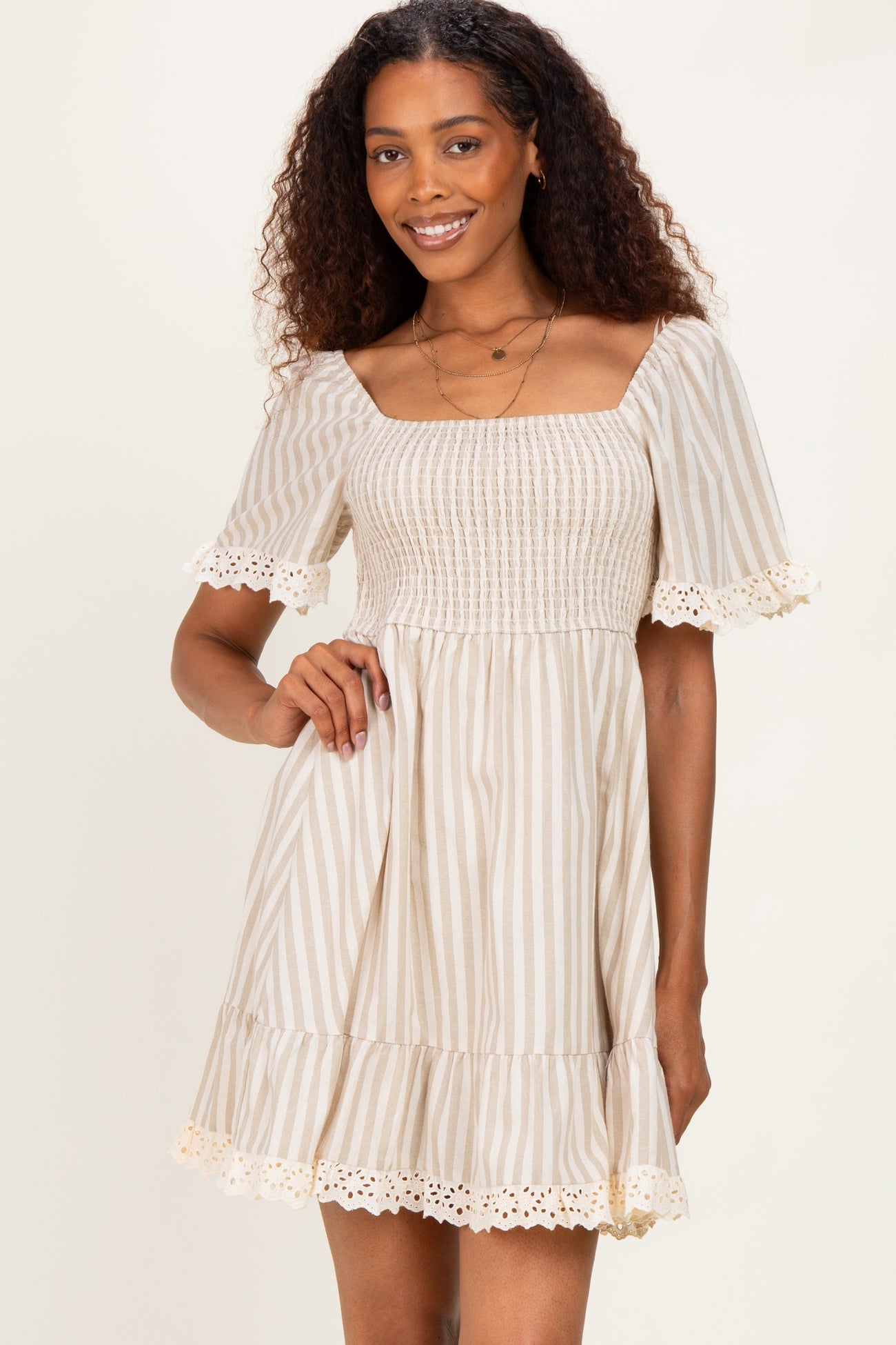 woman wearing a beige and white striped short sleeve dress with a smocked bodice and lace trim at the hem