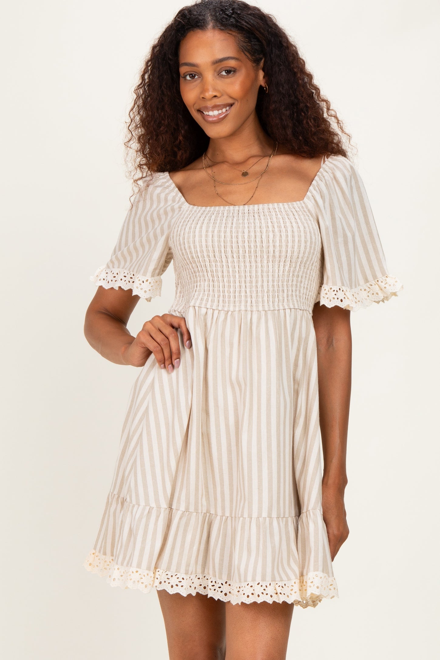 woman wearing a beige and white striped short sleeve dress with a smocked bodice and lace trim at the hem