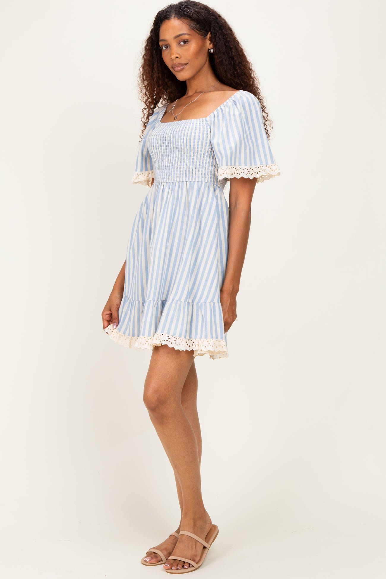 woman wearing a blue and white striped short dress with lace trim and a smocked bodice, standing sideways