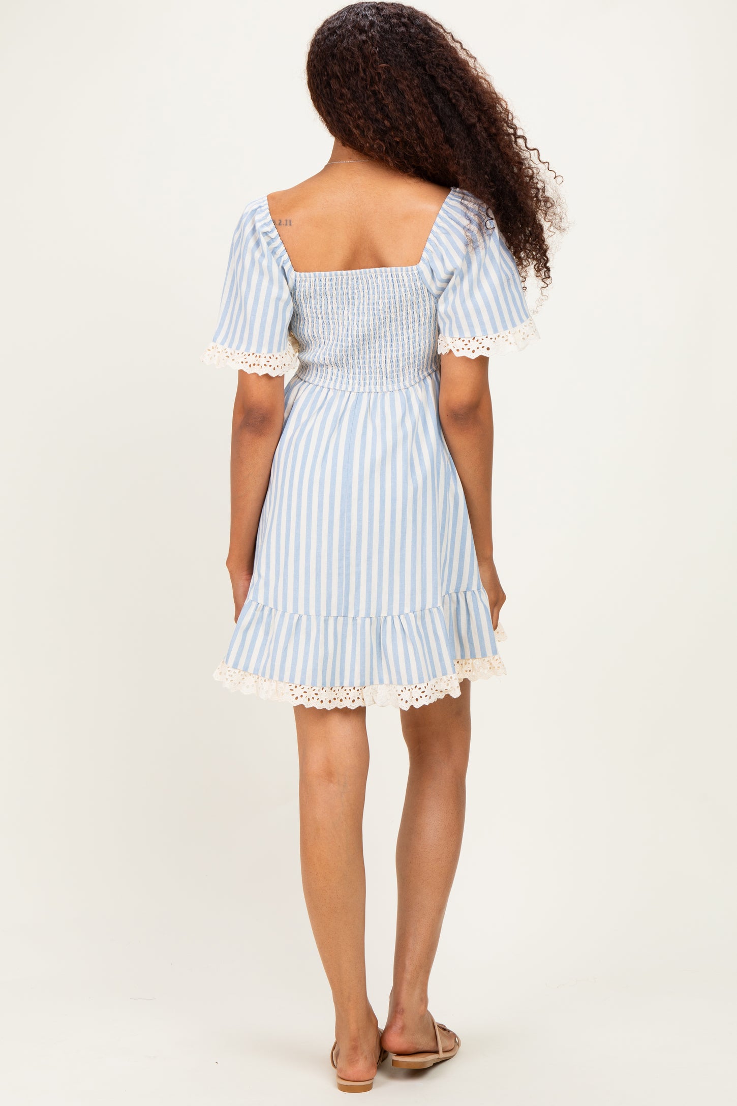 woman wearing a light blue and white striped smocked dress with short sleeves and lace trim